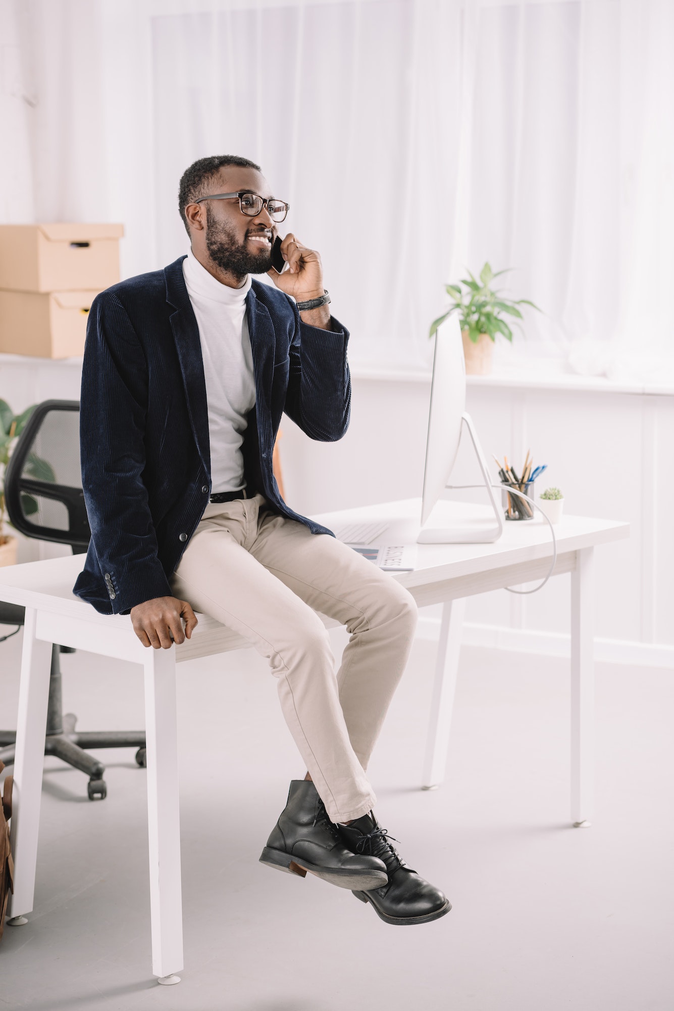 professional african american businessman talking smartphone on while sitting on table in modern